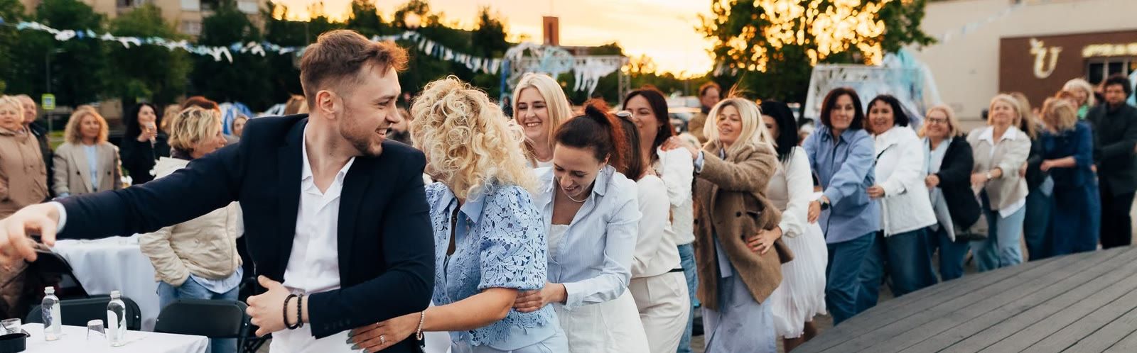 Bachata Utena dalyviai šoka ir juokiasi vakarėlyje lauke saulėlydžio metu